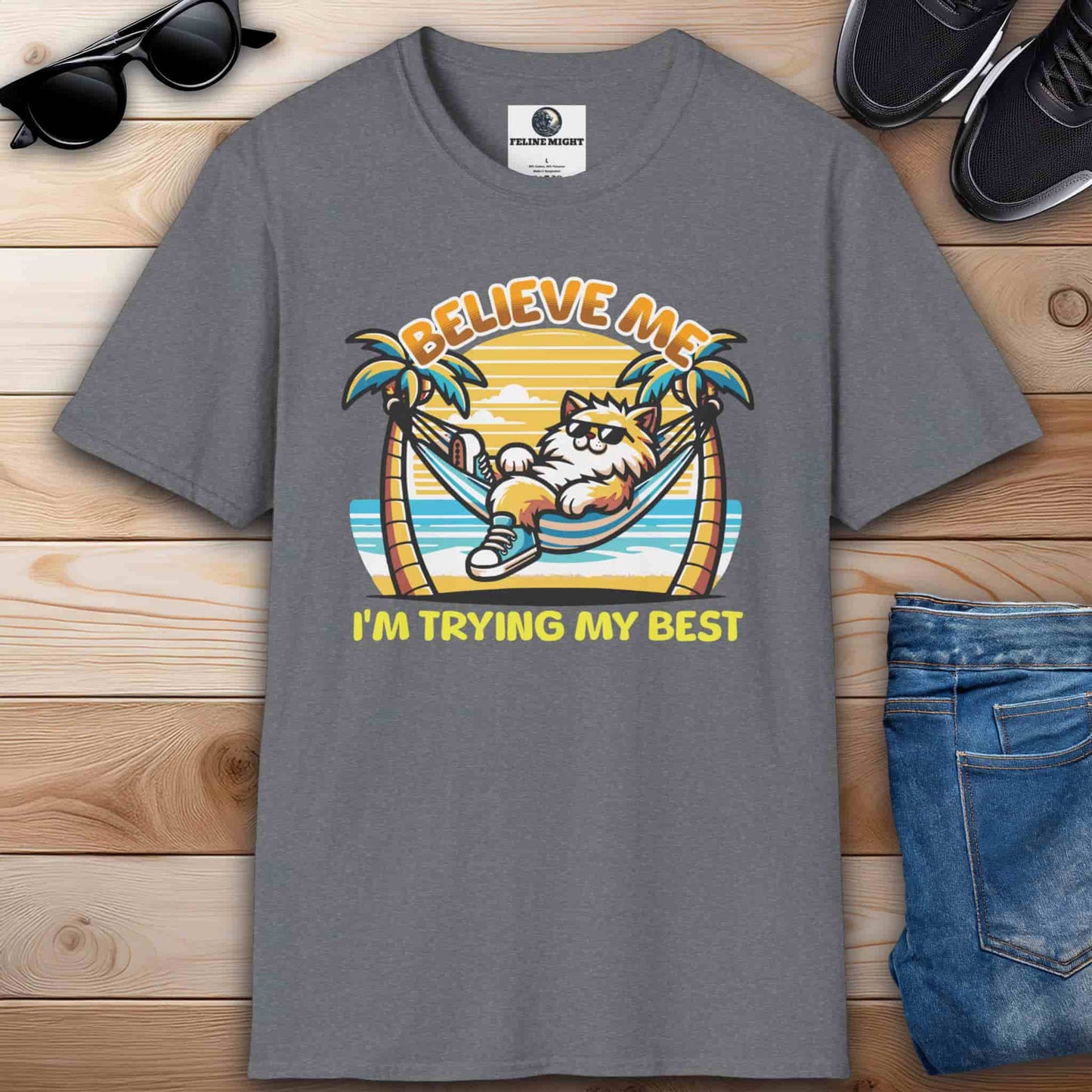 An athletic heather grey t-shirt featuring a cartoon cat relaxing in a hammock with palm trees and the text 'Believe Me I'm Trying My Best'.
