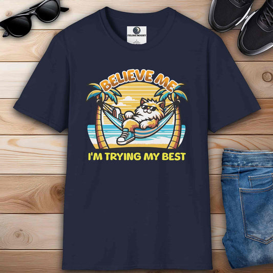 A navy blue t-shirt featuring a cartoon cat relaxing in a hammock with palm trees and the text 'Believe Me I'm Trying My Best'.