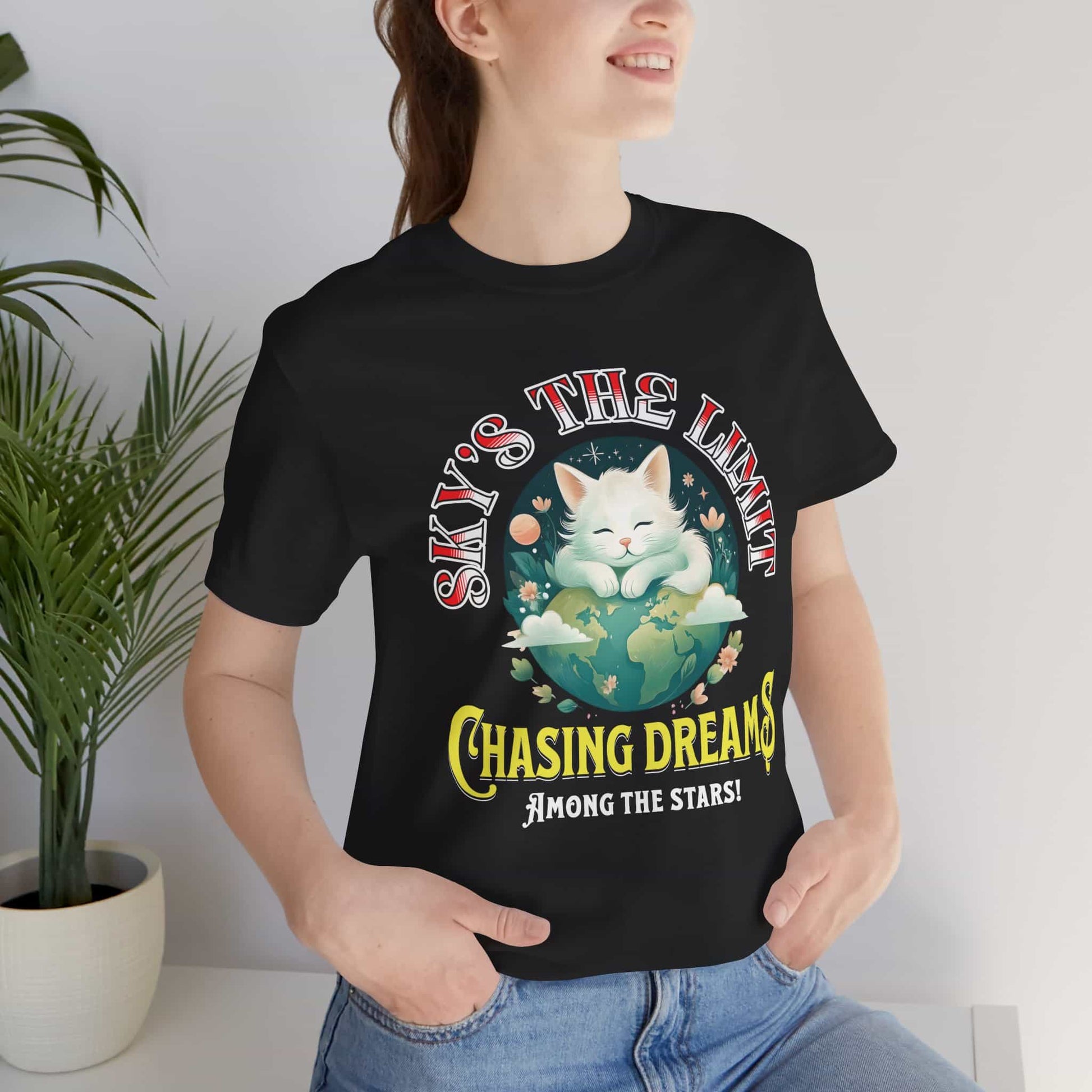 Woman wearing a black Chasing Dreams Cat T-Shirt featuring a motivational design with a cat and the phrase 'Sky's the Limit'.
