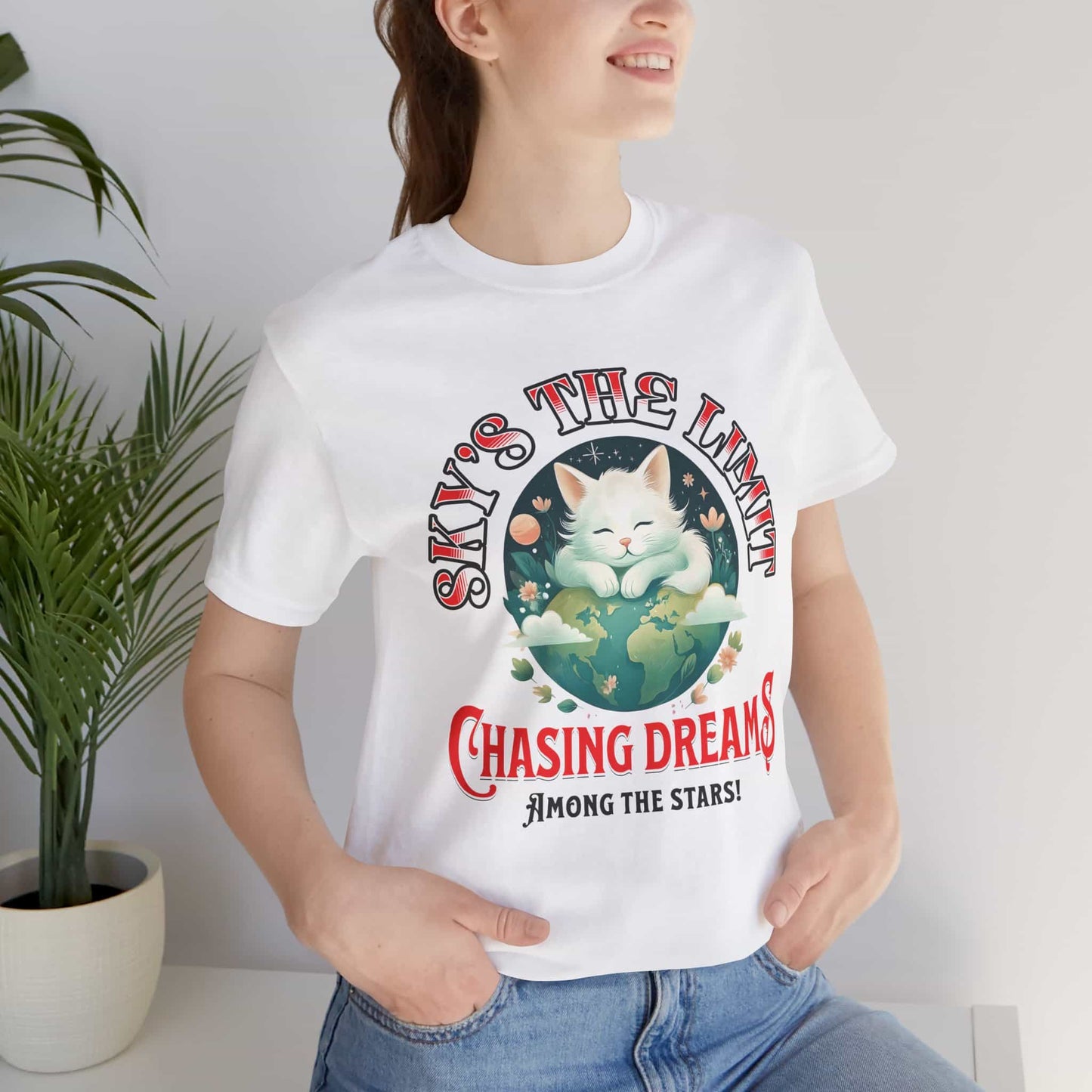 Woman wearing a white Chasing Dreams Cat T-Shirt featuring a motivational design with a cat and the phrase 'Sky's the Limit'.