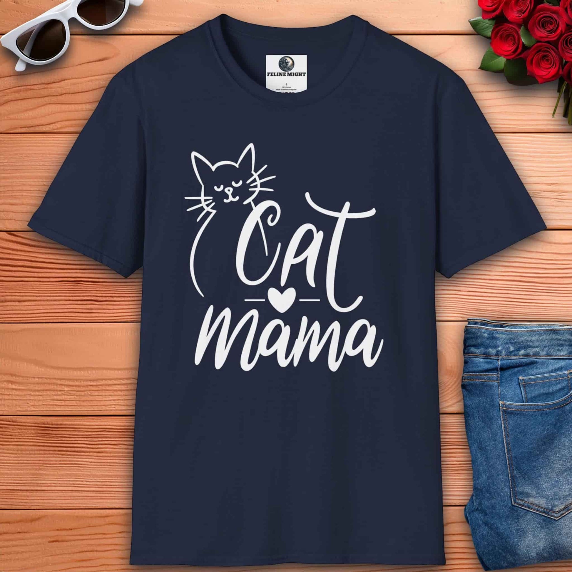 A navy blue Cute Cat Mama T-shirt with 'Cat Mama' design on a wooden surface with sunglasses and flowers.