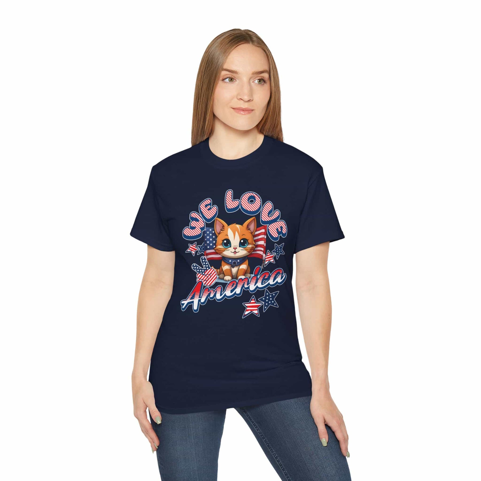 A woman wearing a navy blue Cute Patriotic Cat T-Shirt featuring a cheerful cat illustration in red, white, and blue with the text “We Love America.”