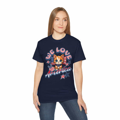 A woman wearing a navy blue Cute Patriotic Cat T-Shirt featuring a cheerful cat illustration in red, white, and blue with the text “We Love America.”