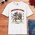 A white Fearless Lioness Women's T-Shirt featuring a sword-wielding queen and lion design on a wooden surface with sunglasses and jeans.