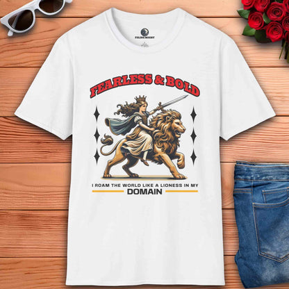 A white Fearless Lioness Warrior T-Shirt featuring a sword-wielding queen and lion design on a wooden surface with sunglasses and jeans.