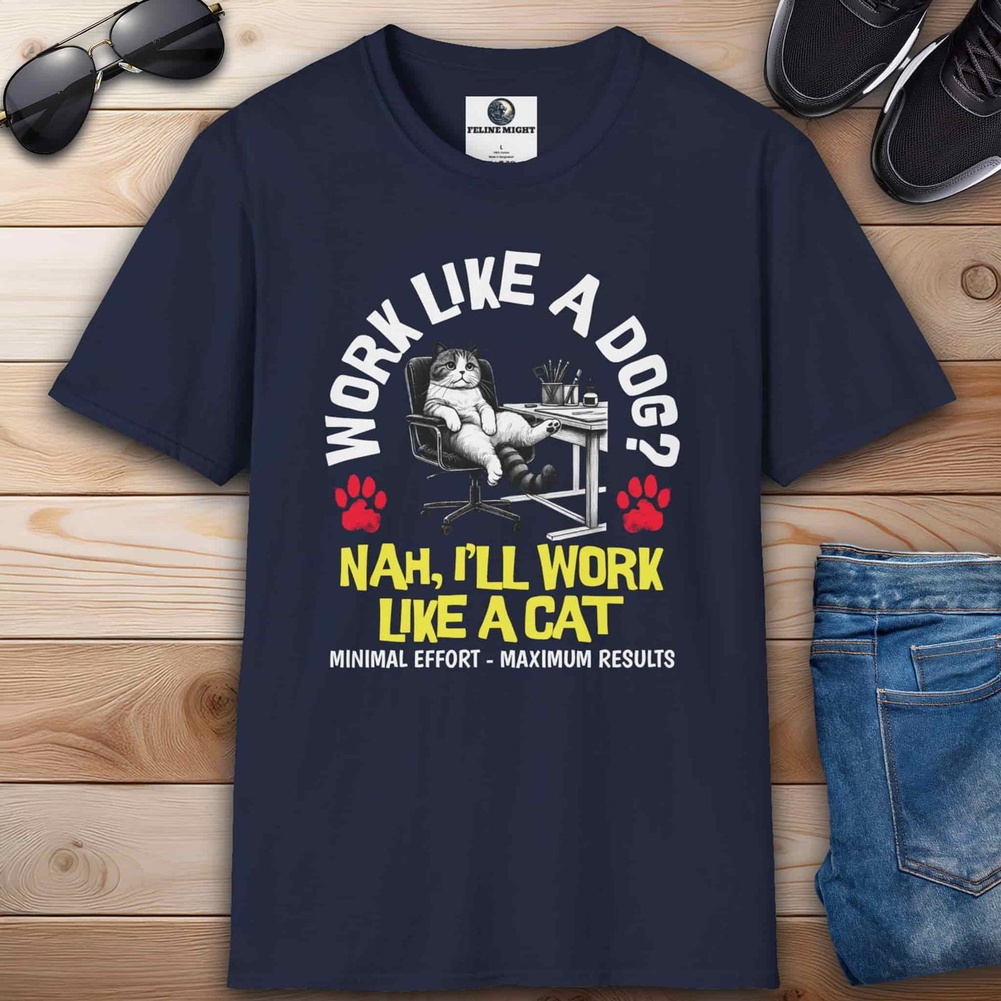 A navy blue Funny Work Cat T-Shirt with a humorous cat graphic and the text 'Work like a dog? Nah, I'll work like a cat,' on a wooden surface with sunglasses and jeans.