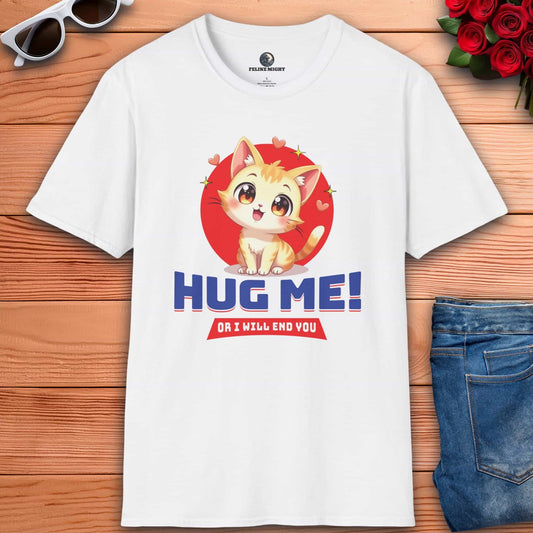 White t-shirt with a cartoon cat and text: "Hug Me! Or I will end you." Surrounded by hearts, laid on a wooden surface next to sunglasses, a red rose bouquet, and blue jeans.