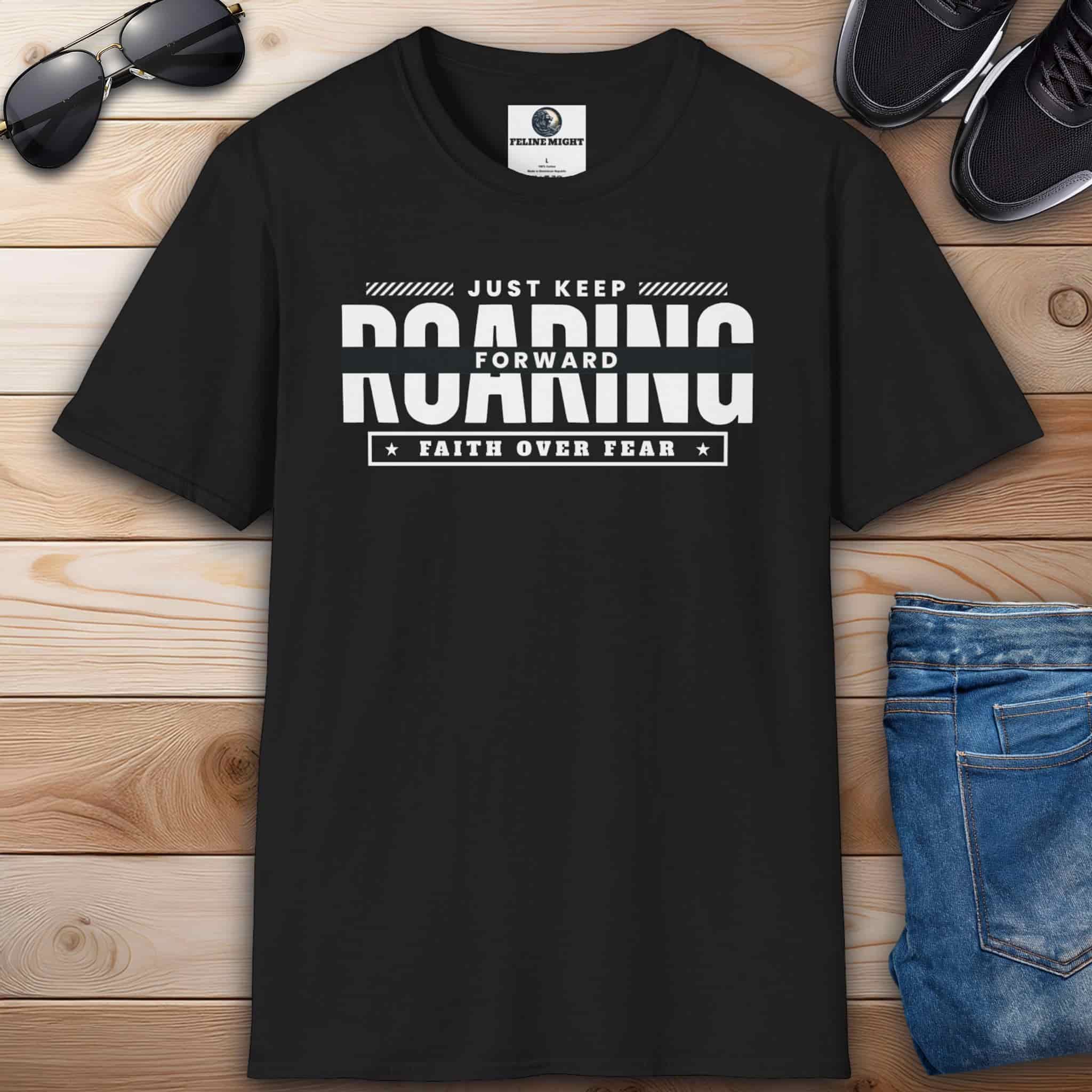 A black Just Keep Roaring Forward Quote Tee displayed on a wooden surface with sunglasses, sneakers, and jeans.