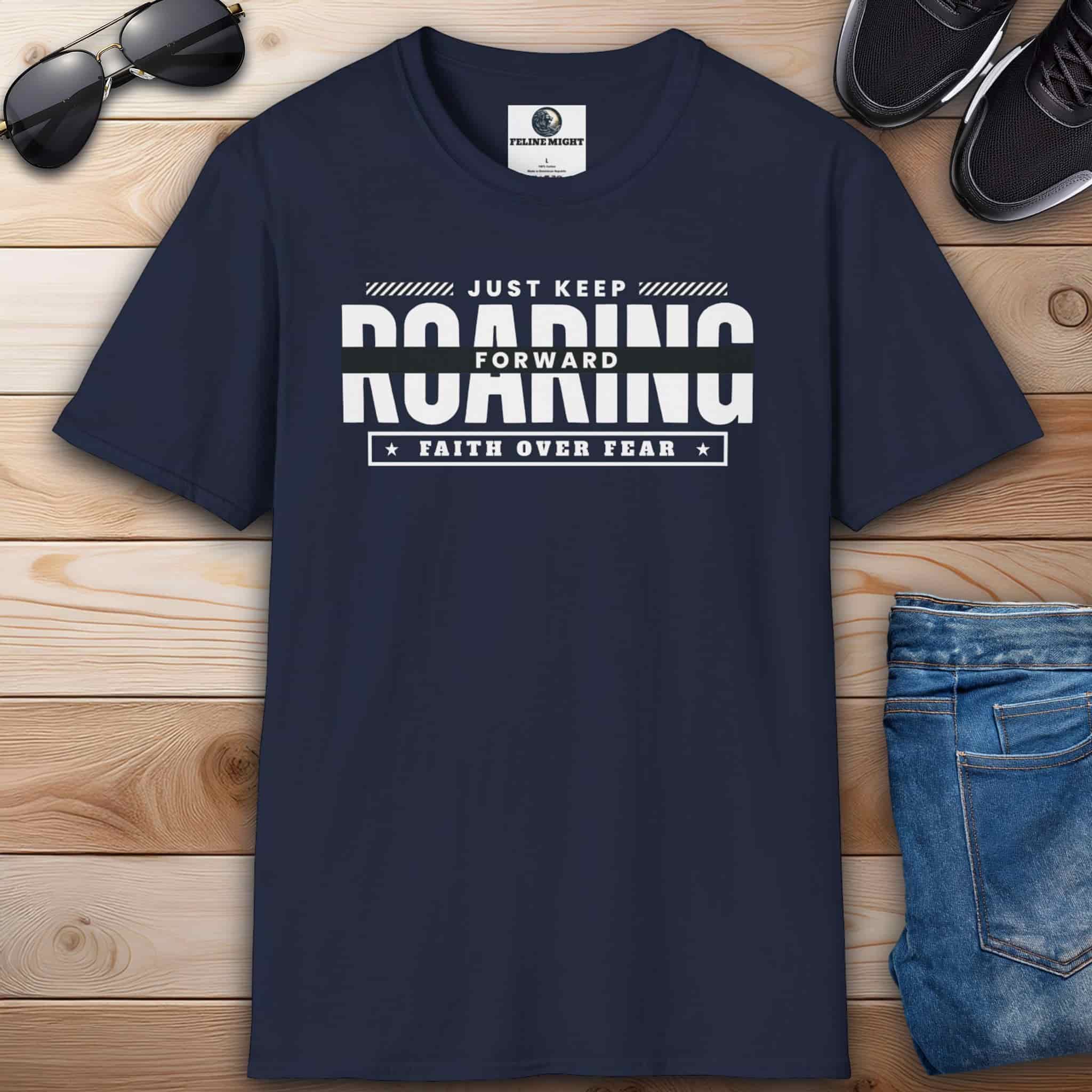 A navy blue Just Keep Roaring Forward Quote Tee displayed on a wooden surface with sunglasses, sneakers, and jeans.