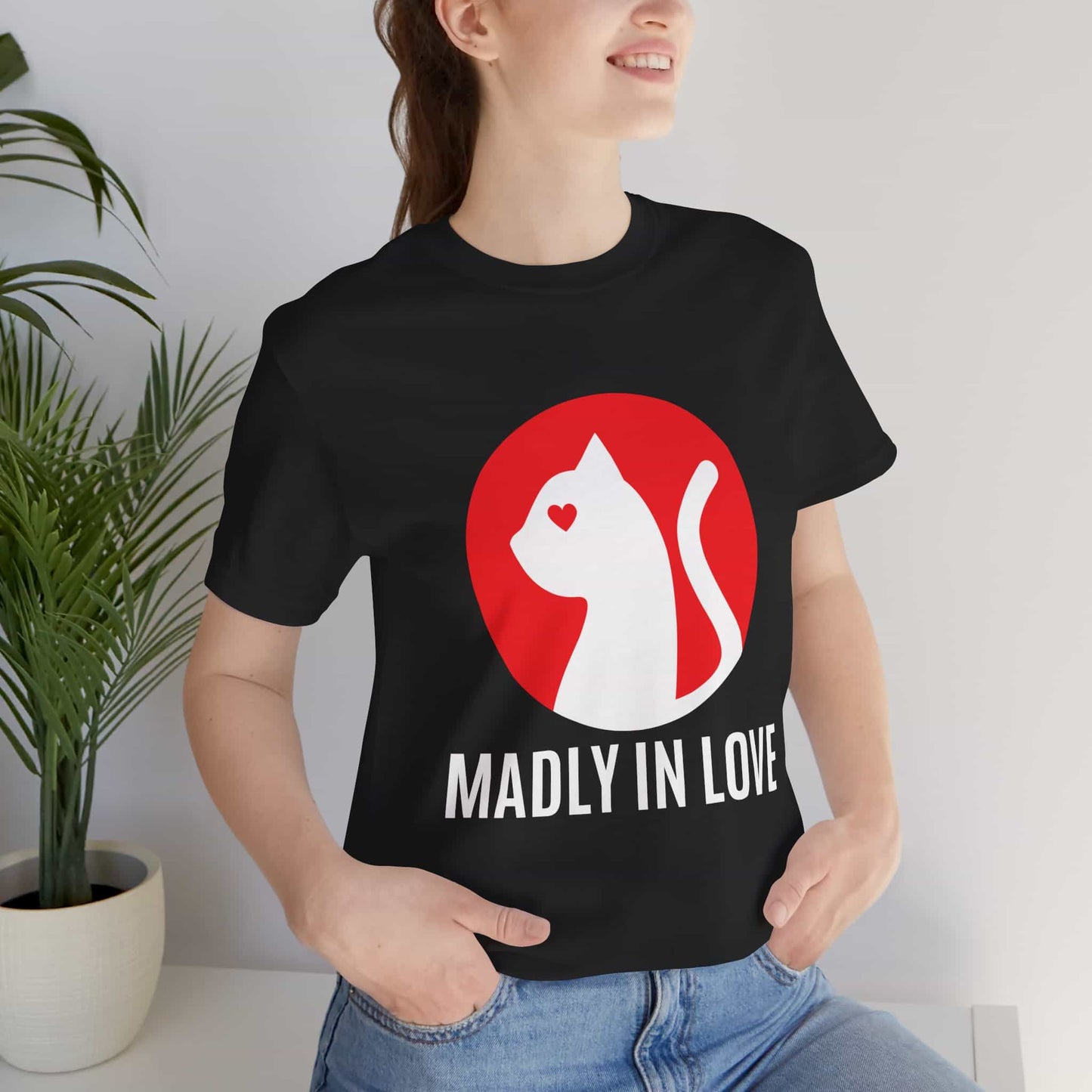 A woman in a black Madly in Love Cat T-Shirt featuring a cat silhouette on a red circle, a perfect romantic gift for cat lovers.