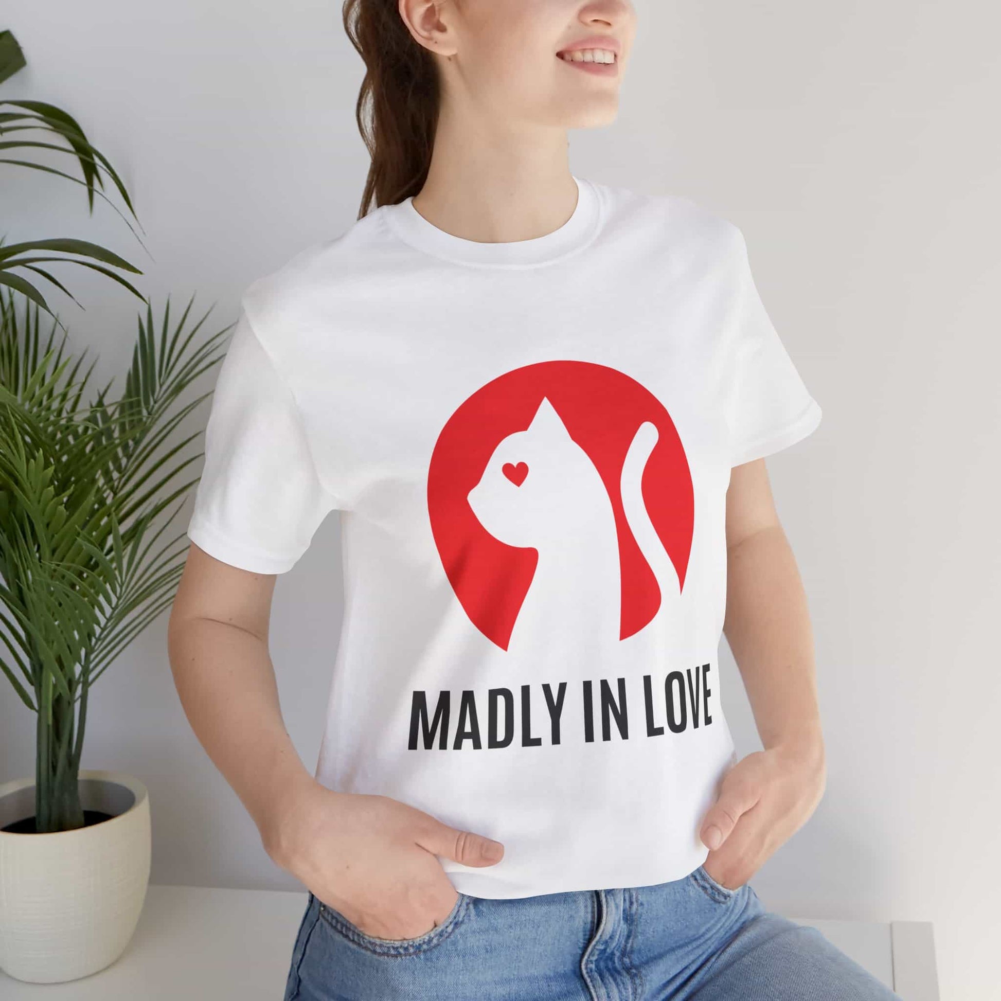A woman in a white Madly in Love Cat T-Shirt featuring a cat silhouette on a red circle, a perfect romantic gift for cat lovers.