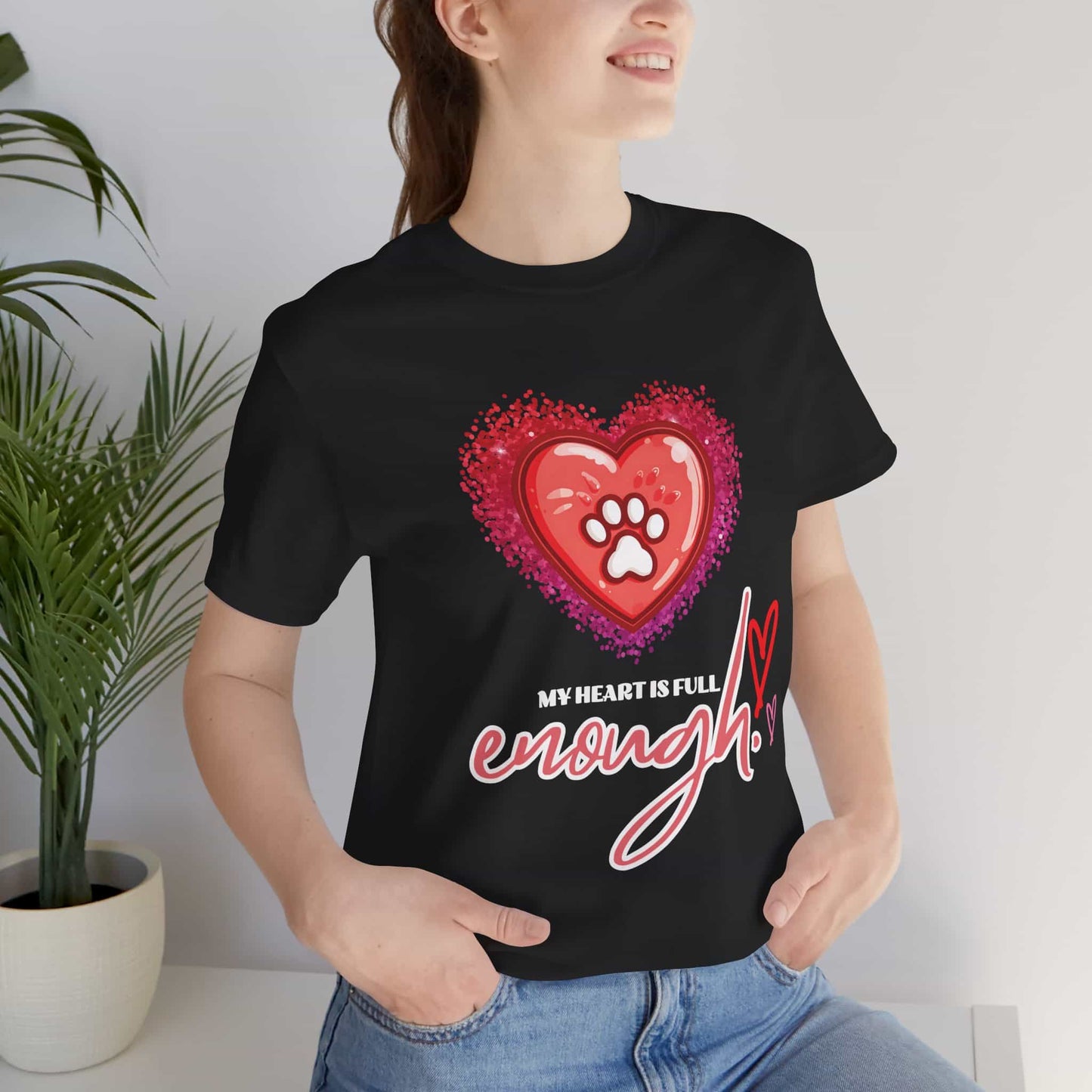 A person wearing a black My Heart is Full Cat T-shirt with a heart and paw print design, standing indoors next to a plant.