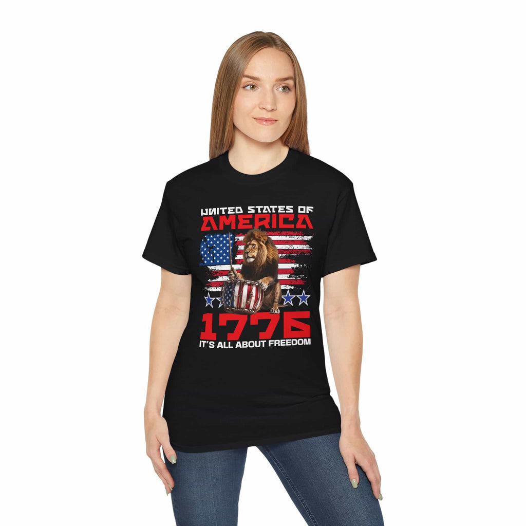 A woman wearing a black It's All About Freedom T-Shirt featuring a drum-playing lion, the American flag, and the text 'It's All About Freedom'.