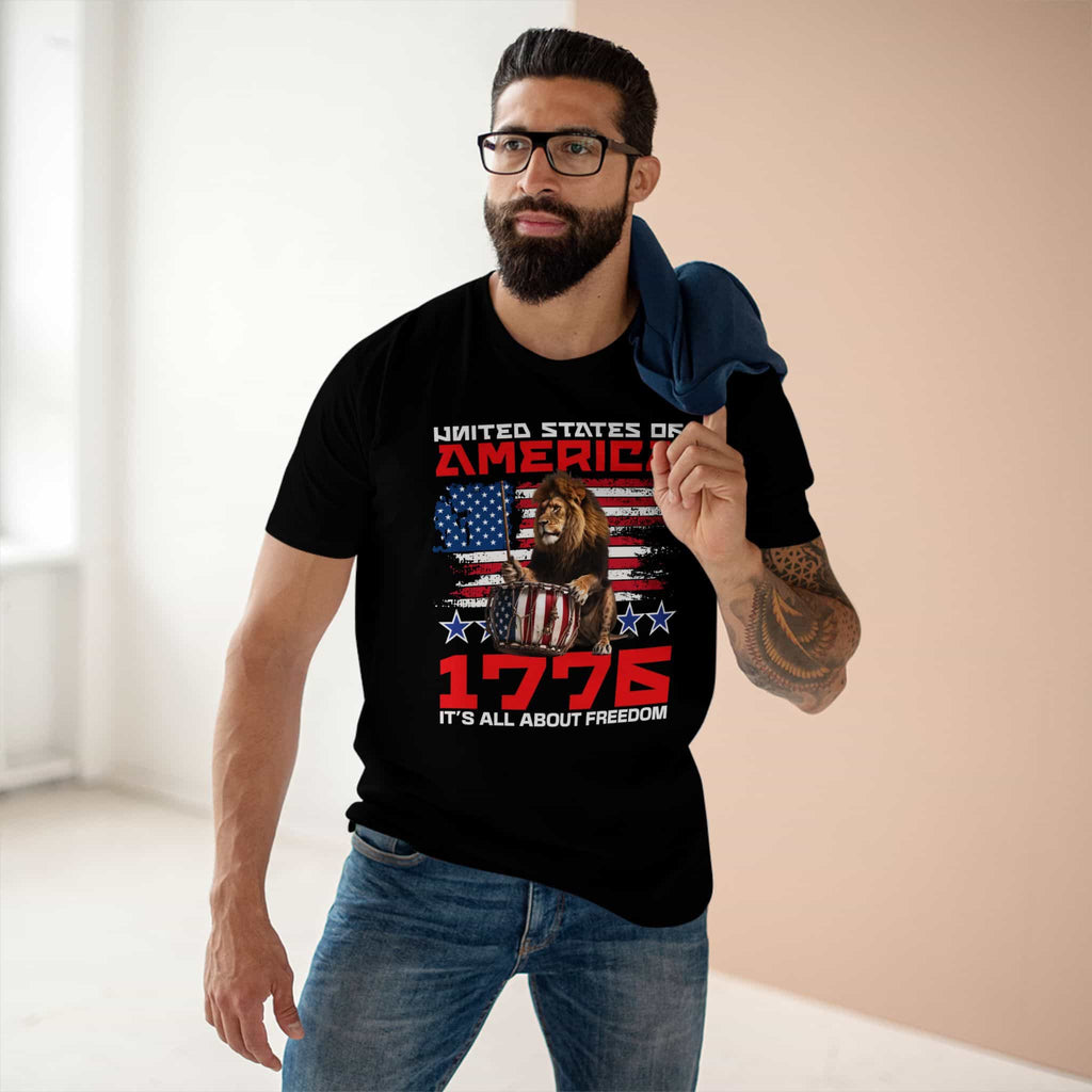 A man wearing a black It's All About Freedom T-Shirt, featuring a drum-playing lion, the American flag, and the text 'It's All About Freedom'.