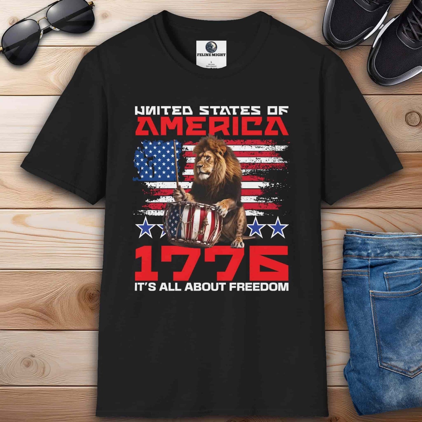 A black Patriotic Lion Freedom T-Shirt featuring a drum-playing lion and the American flag with text '1776 It's All About Freedom'.