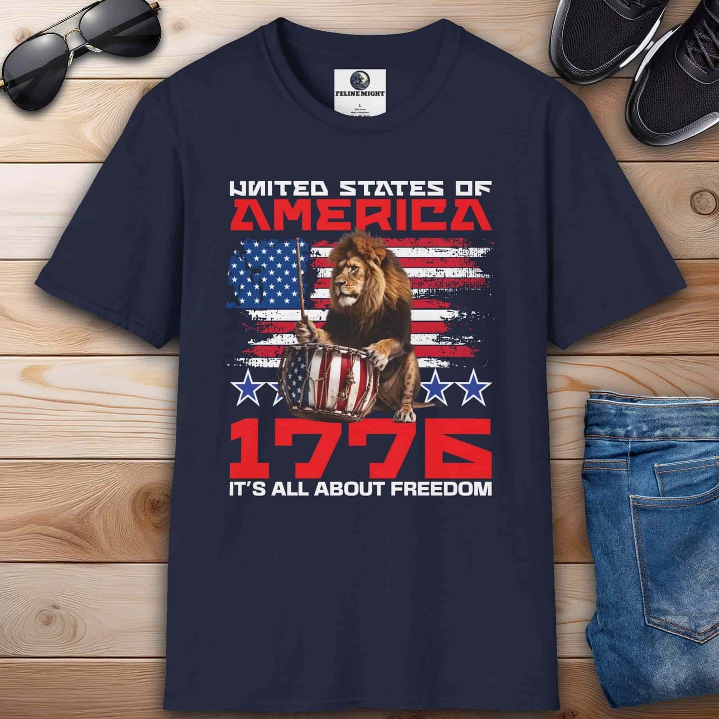 A navy blue Patriotic Lion Freedom T-Shirt featuring a drum-playing lion and the American flag with text '1776 It's All About Freedom'.