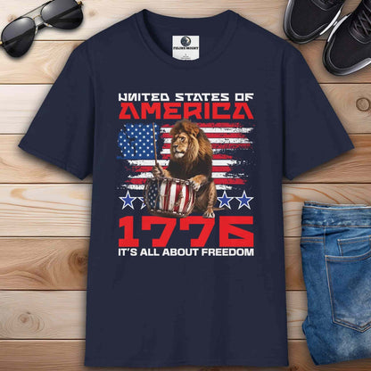 A navy blue Patriotic Lion Freedom T-Shirt featuring a drum-playing lion and the American flag with text '1776 It's All About Freedom'.