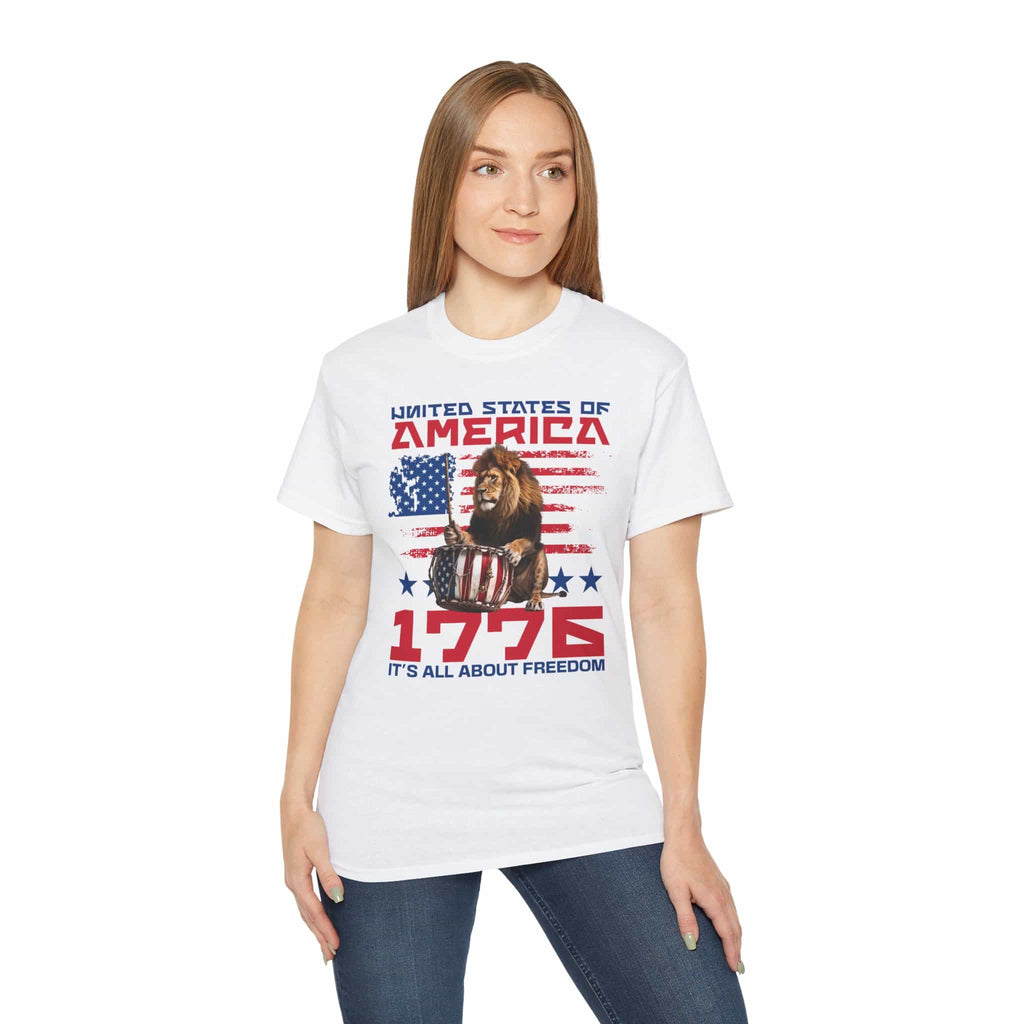 A woman wearing a white It's All About Freedom T-Shirt, featuring a drum-playing lion, the American flag, and the text 'It's All About Freedom'.