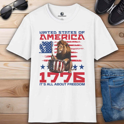 A white Patriotic Lion Freedom T-Shirt featuring a drum-playing lion and the American flag with text '1776 It's All About Freedom'.