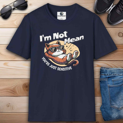 A navy blue Sarcastic Cat Humor T-Shirt with a graphic of a cat wearing sunglasses and the text 'I'm Not Mean, You're Just Sensitive', on a wooden surface with shoes and jeans.