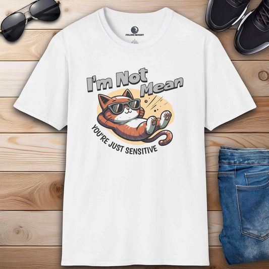 A white Sarcastic Cat Humor T-Shirt with a graphic of a cat wearing sunglasses and the text 'I'm Not Mean, You're Just Sensitive', on a wooden surface with shoes and jeans.