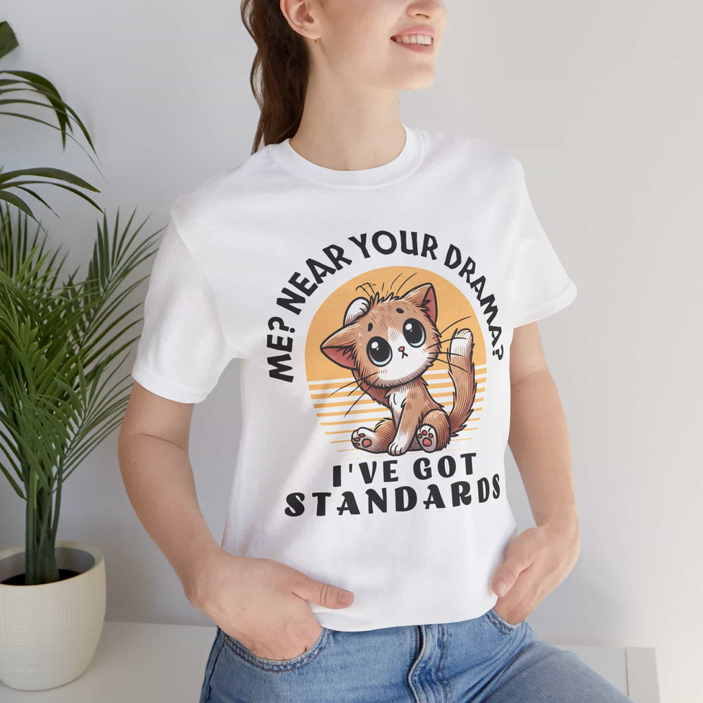 A woman wearing a white Sassy Cat Graphic T-Shirt featuring a humorous design with a cute cat and text saying 'Me? Near Your Drama? I've Got Standards.'