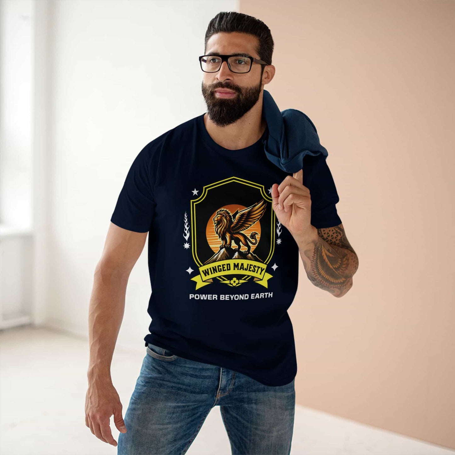 A man wearing a navy blue Winged Majesty Lion T-Shirt featuring a golden-winged lion graphic and the text 'Power Beyond Earth', standing indoors.